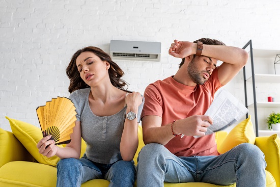 pretty woman with hand fan and handsome man with newspaper suffering from heat at home