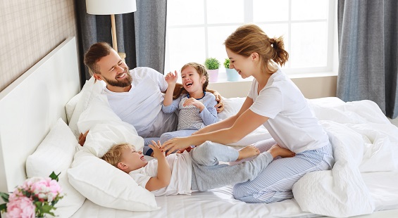 happy family mother, father and children laughing, playing and tickles in bed in bedroom at home