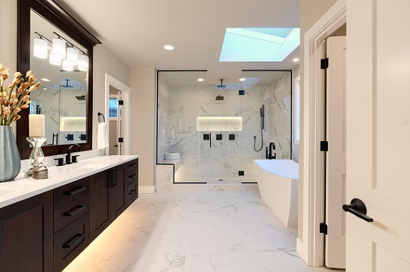Luxury modern home bathroom interior with dark brown cabinets, white marble, walk in shower, free standing tub, two mirrors, flowers.