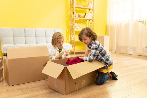 Excited kids laughing playing in new home carrying boxes, happy family with children enjoying relocation, small girl and boy having fun in living room helping parents to pack, moving day concept. Family