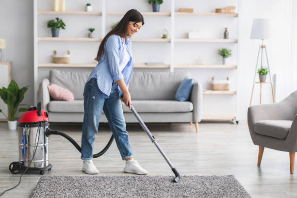Housekeeping, Home Routine Concept. Full body length portrait of happy young casual lady using vacuum cleaner, cleaning rug floor carpet, removing dust in modern living room, free copy space