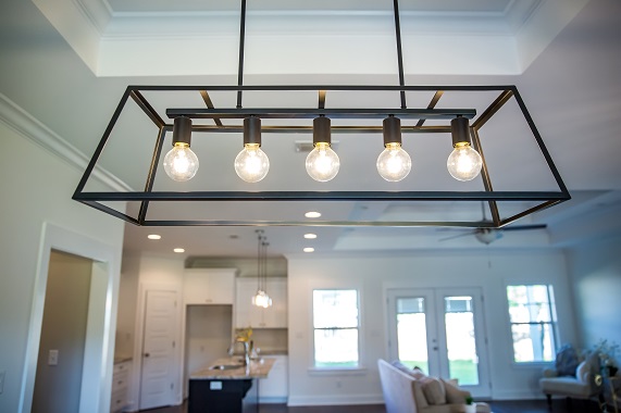 Hanging retro black metal iron chandelier lighting fixture with vintage bulbs hanging in a dining room of a new construction house